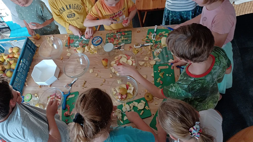 Viele Kinder um einen Tisch schneiden Äpfel und bereiten sie für das Apfelmus vor.