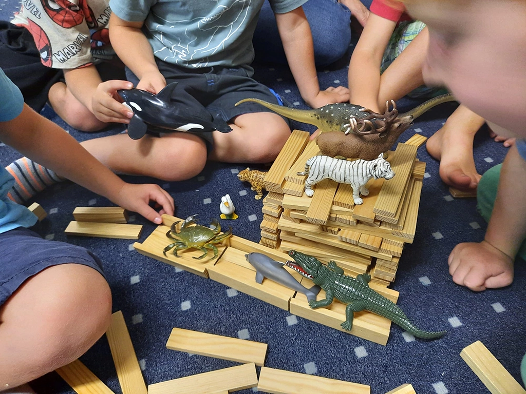 Die Kinder spielen mit Tierfiguren und Holzstapeln.