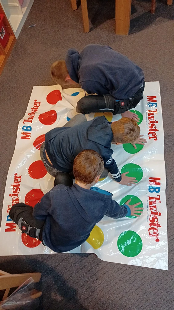 Kinder sitzen auf eienr Folie und spielen Twister.