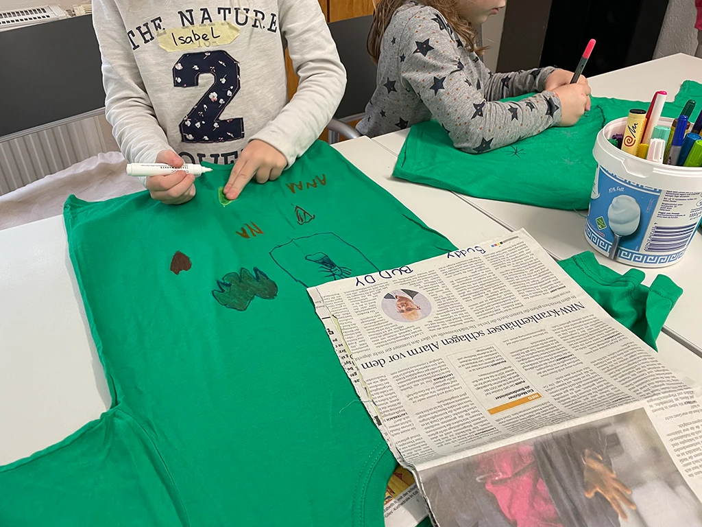 Kinder malen auf einem grünen Shirt.