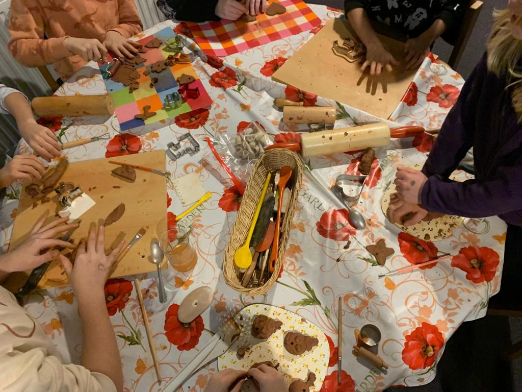 Auf einer bunten Wachstischdecke verarbeiten die Kinder Ton mit den Händen, einem Nudelholz und vielen Kochlöffeln